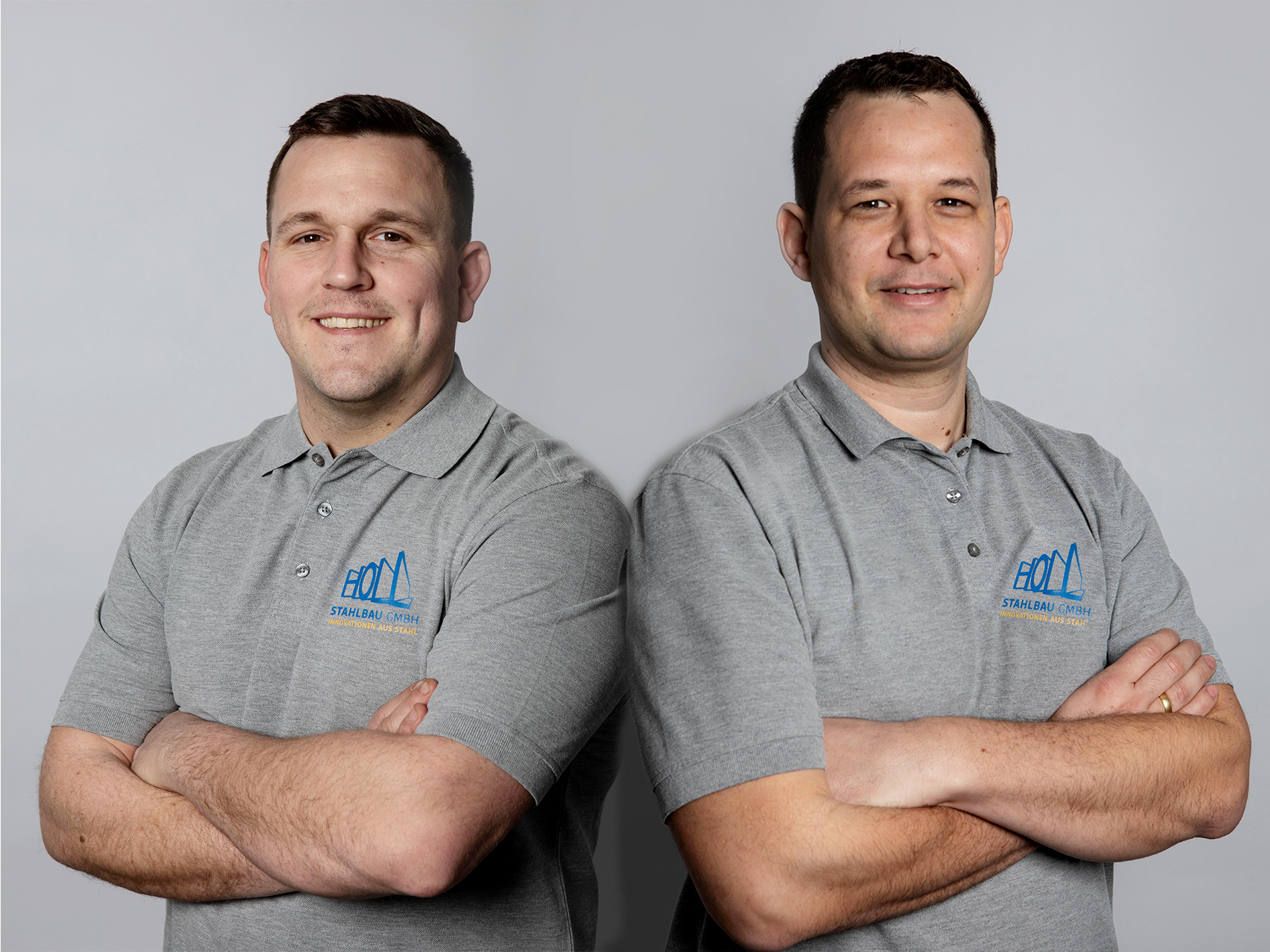 Zwei Männer in grauen Poloshirts mit dem Logo "HOL" stehen nebeneinander mit verschränkten Armen.